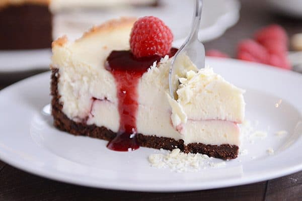 A fork taking a bite out of a slice of a White Chocolate Raspberry Truffle Cheesecake