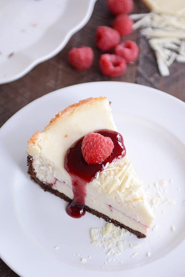 A slice of white chocolate cheesecake topped with raspberry sauce and a raspberry. 
