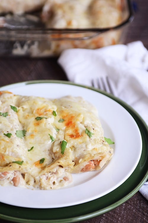 A plate of three baked green chile chicken enchiladas, with a fork and napkin on the side. 