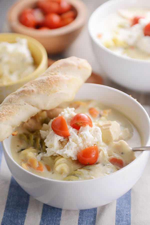 A white bowl of creamy lasagna soup with a breadstick on the side.
