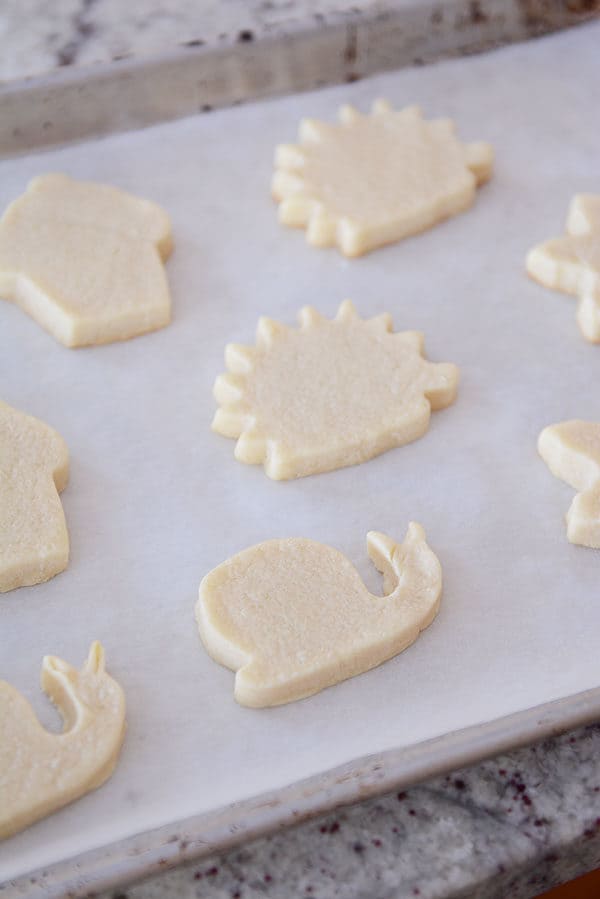 White sugar cookies cut out in various shapes all sitting on a piece of parchment paper. 