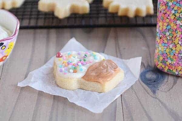 A sugar cookie decorated to look like a cupcake, laying on a white square of parchment paper. 