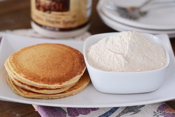 A stack of cooked pancakes next a bowl of ground wheat.