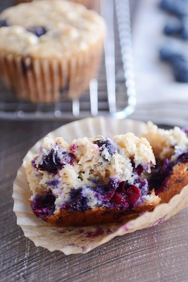 A blueberry muffin split in half on a muffin liner. 