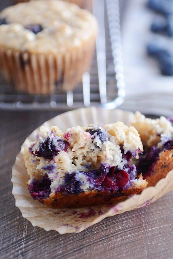 A blueberry muffin split in half on a muffin liner. 