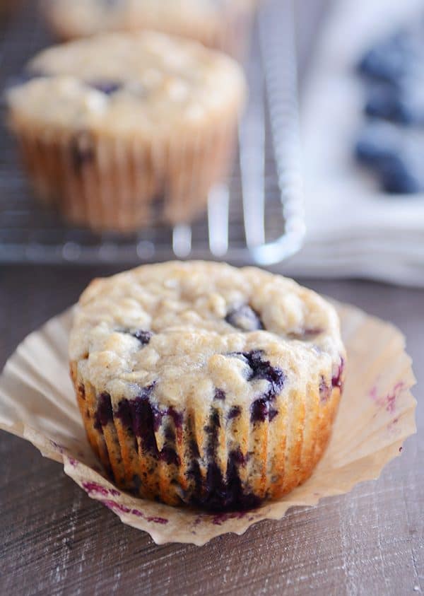 An unwrapped blueberry muffin sitting on a muffin liner. 