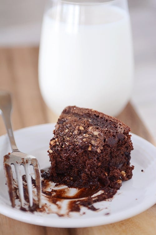 A half-eaten piece of chocolate fudge cake on a white plate with a fork on the side.