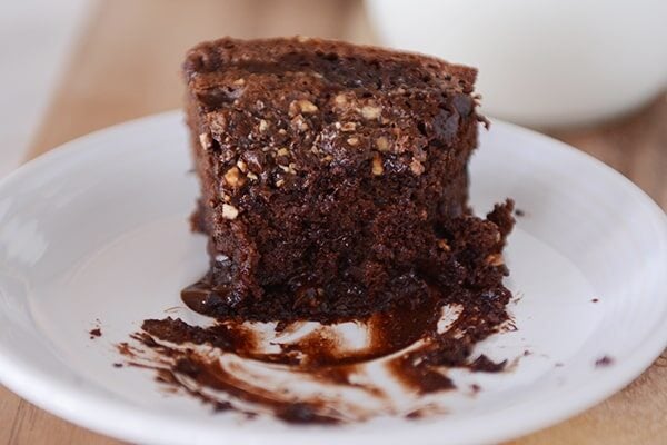 A half-eaten piece of chocolate fudge cake on a white plate.