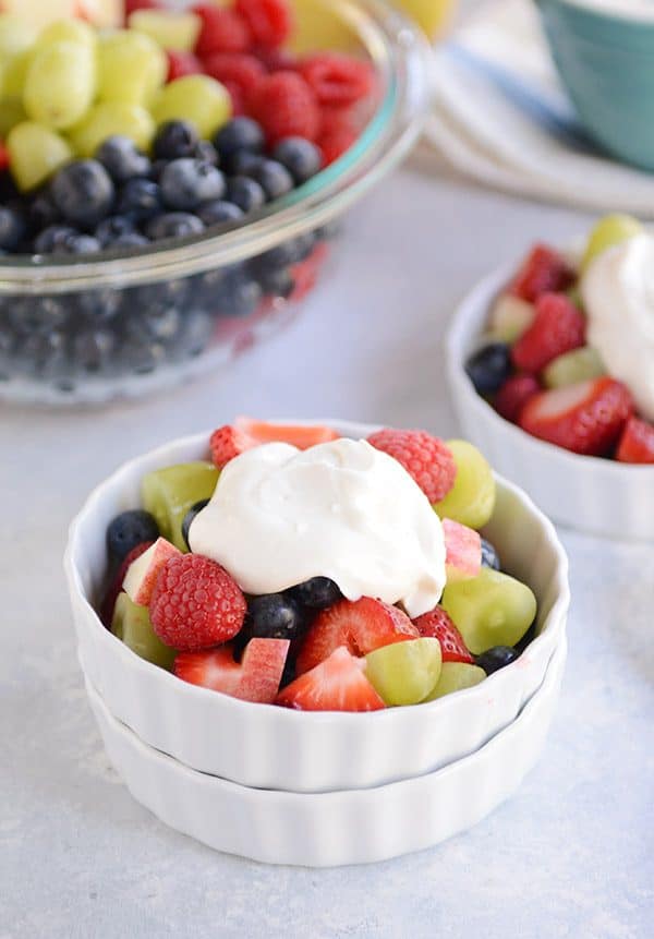 Fruit salad topped with yogurt in a white ramekin.