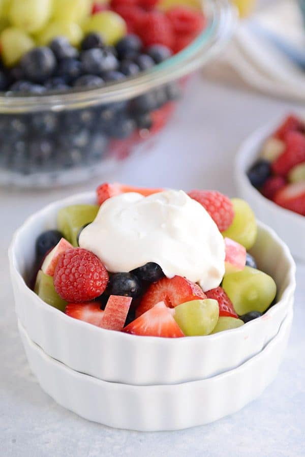 a white bowl full of fresh fruit salad topped with vanilla yogurt