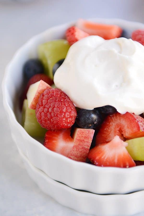 A white bowl full of fresh fruit salad topped with vanilla yogurt.