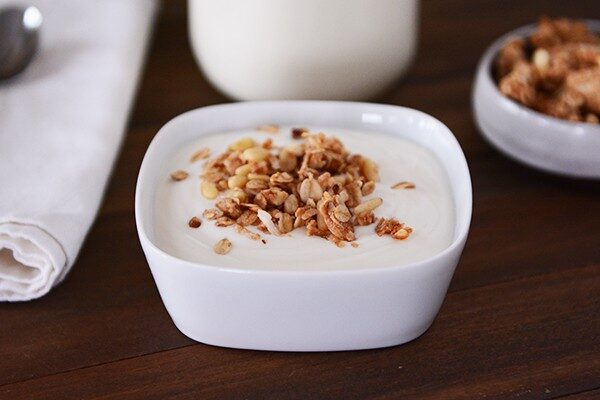 A square white bowl of yogurt topped with granola. 