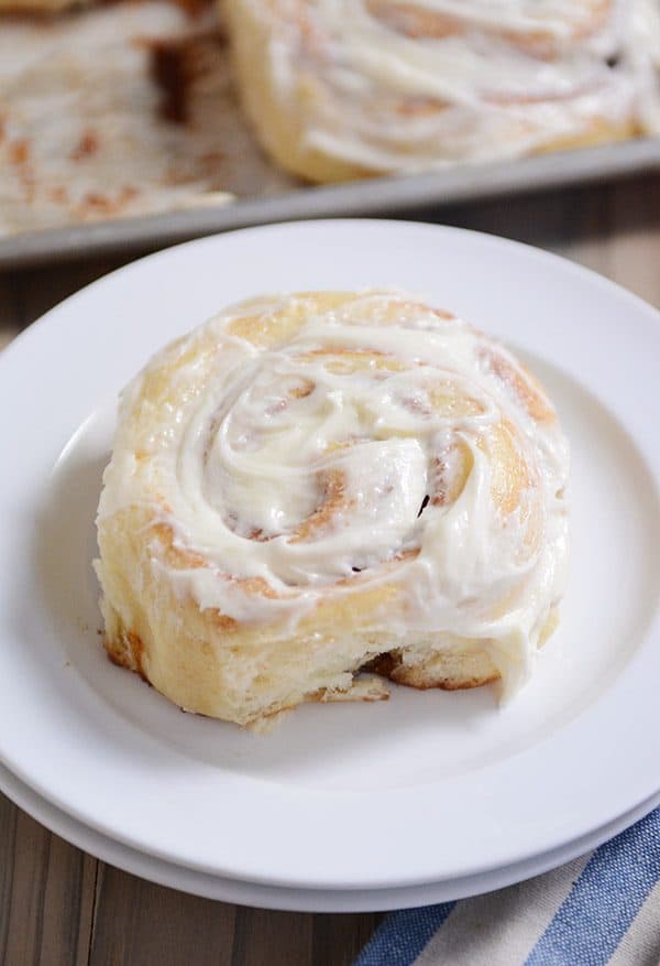 Top view of a frosted cinnamon roll on a white plate. 