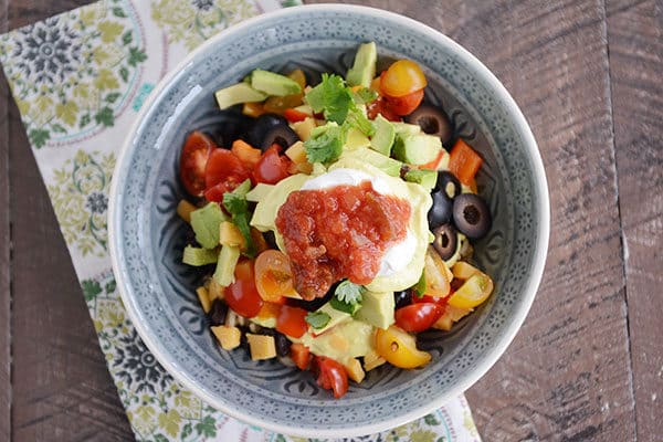 A bowl full of chopped veggies, sliced olives, chopped avocado, tomatoes, cilantro, salsa, and sour cream. 