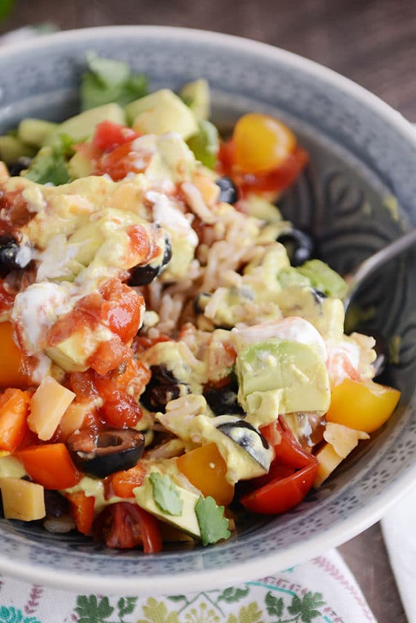 A bowl full of rice, topped with cubes of cheese, sliced olives, chopped avocado, tomatoes, and salsa.