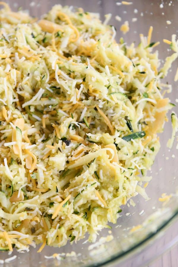 A glass bowl of shredded zucchini and cheese and mixed together. 