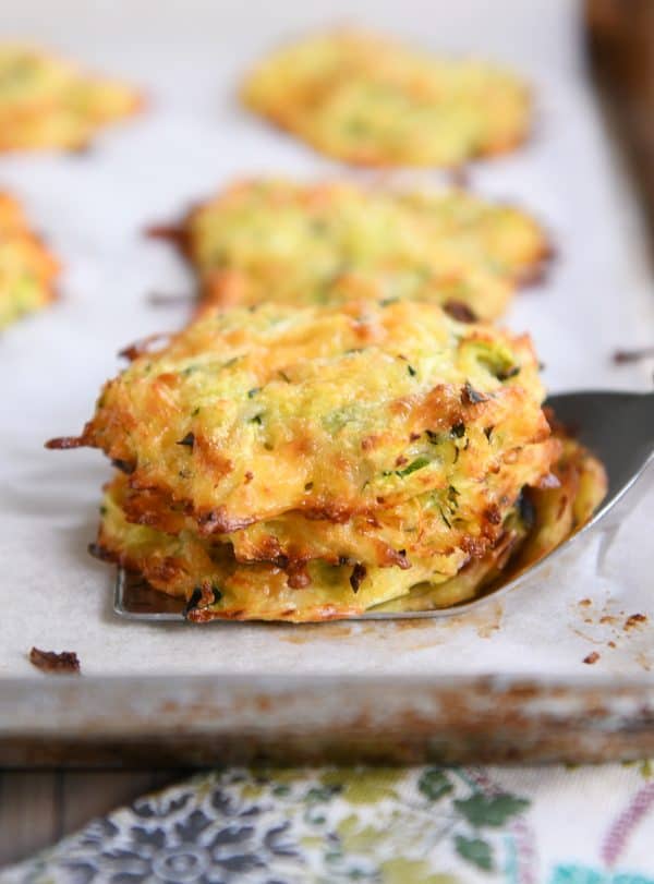 Baked cheesy zucchini bites stacked on a spatula.