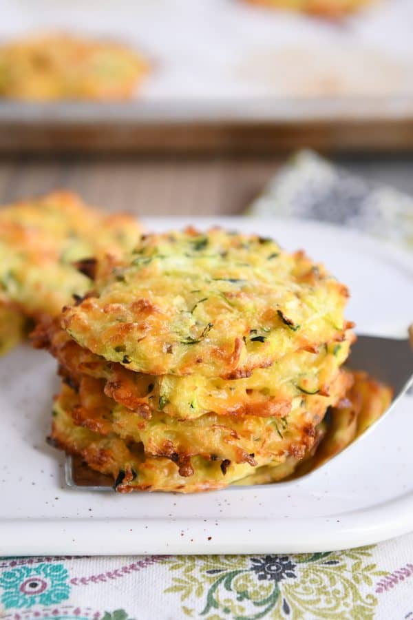 Four baked cheesy zucchini bites stacked on a spatula.