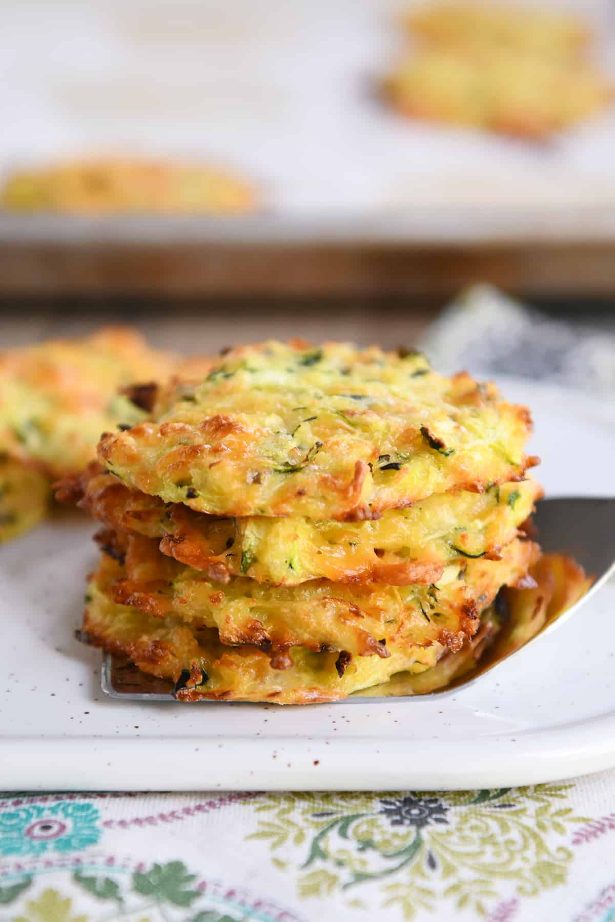 Cheesy baked zucchini bites stacked on a spatula.