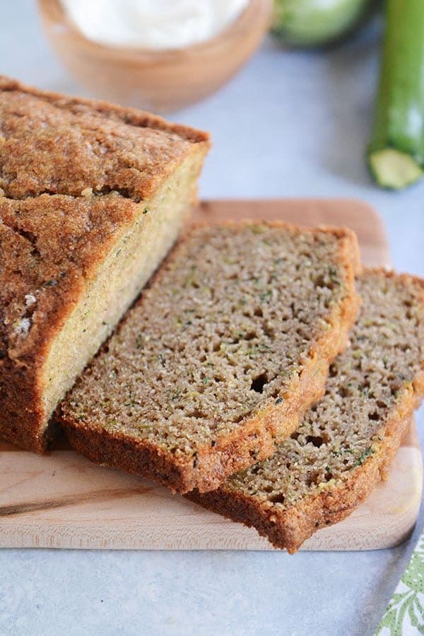 A loaf of zucchini bread with two slices cut off on a wooden cutting board.