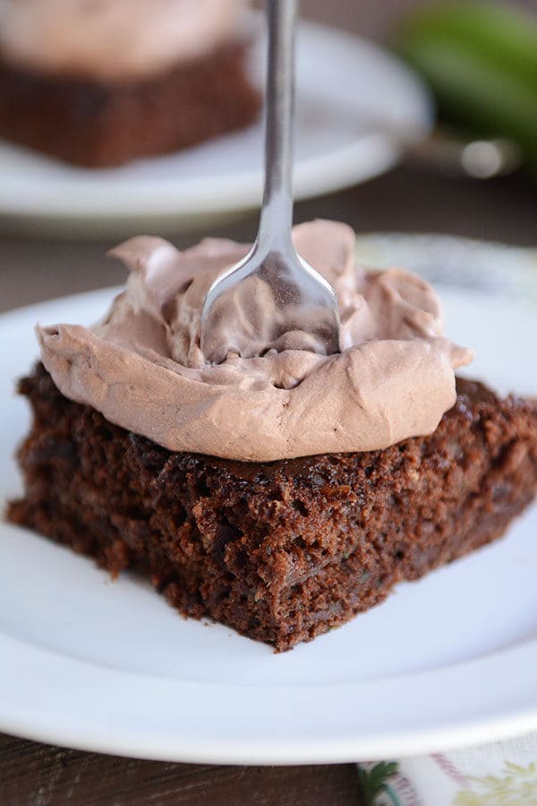 A fork sticking into a piece of chocolate cake with whipped chocolate frosting.