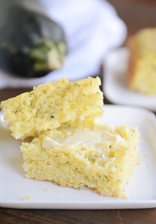 A big piece of zucchini cornbread cut in half with butter on one half.