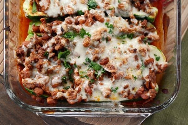 Top view of a glass casserole dish full of cheesy stuffed zucchini boats.