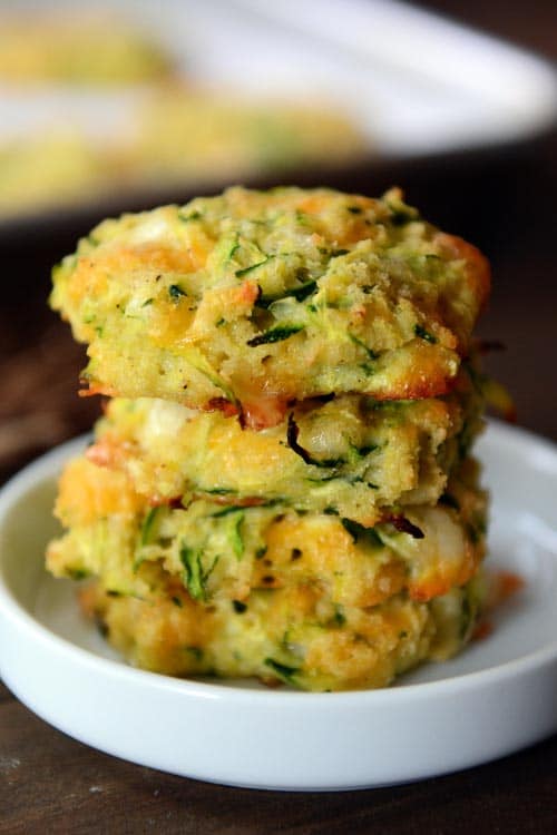 Four Baked Cheesy Zucchini Bites stacked on a small white ramekin. 