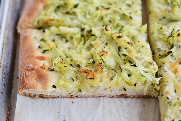 Cut up zucchini-topped pizza on a cookie sheet.