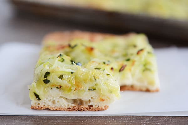 A piece of zucchini-topped pizza with a bite taken out.